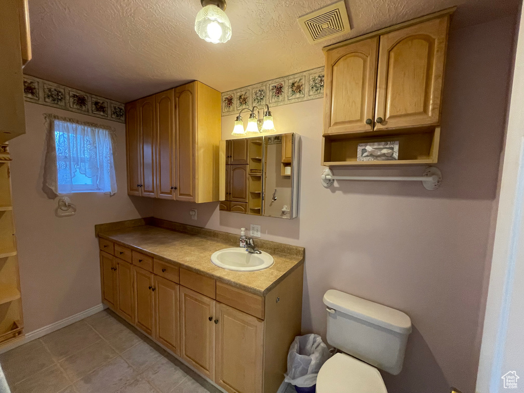 Bathroom featuring visible vents, toilet, vanity, and a textured ceiling