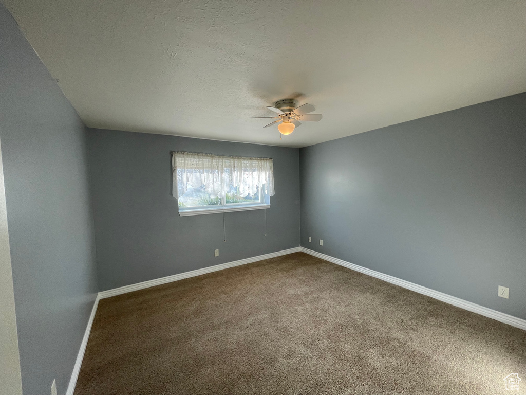 Unfurnished room featuring dark carpet, baseboards, and a ceiling fan