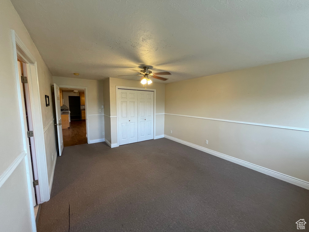 Unfurnished bedroom featuring a textured ceiling, a closet, a ceiling fan, dark colored carpet, and baseboards