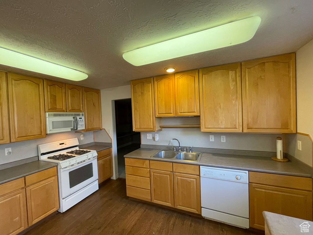 Kitchen with a sink, white appliances, dark wood-type flooring, and a textured ceiling