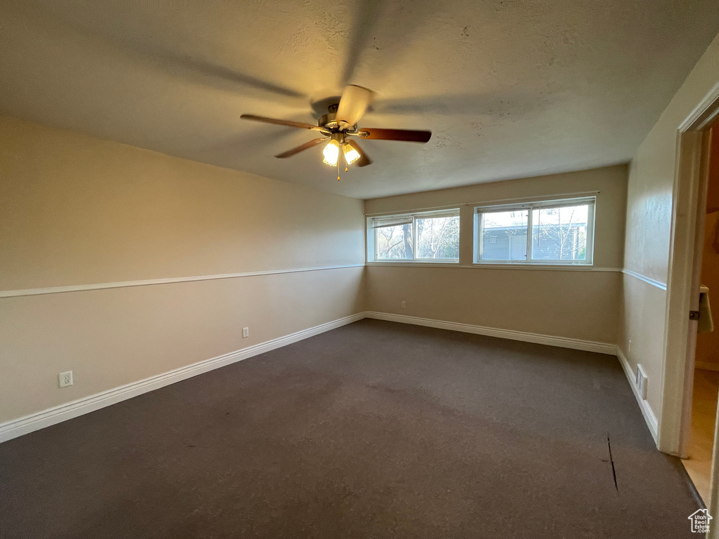 Empty room with dark carpet, baseboards, a ceiling fan, and visible vents