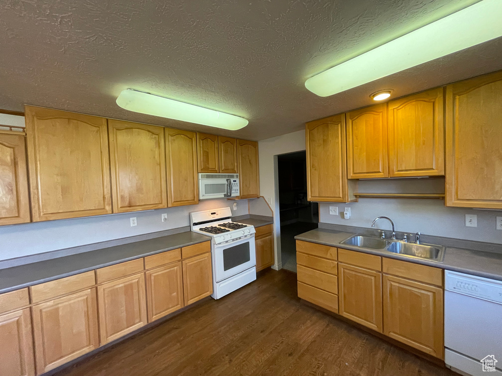 Kitchen with a textured ceiling, dark wood-style flooring, a sink, and white appliances