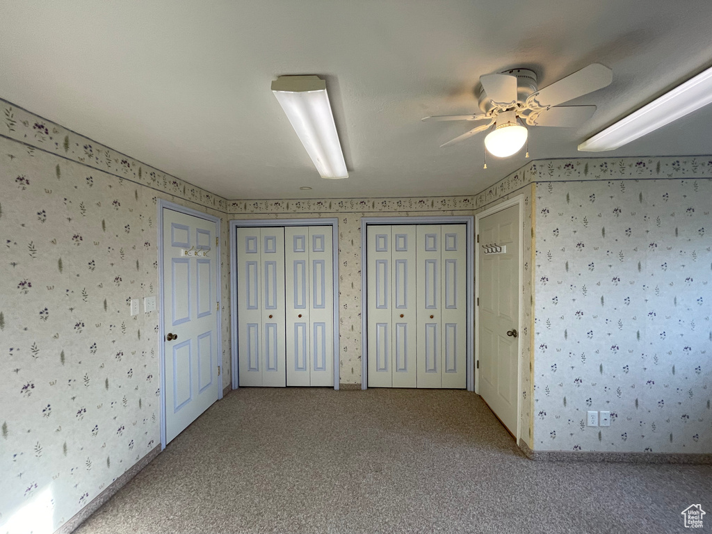 Unfurnished bedroom with wallpapered walls, carpet flooring, a ceiling fan, and multiple closets