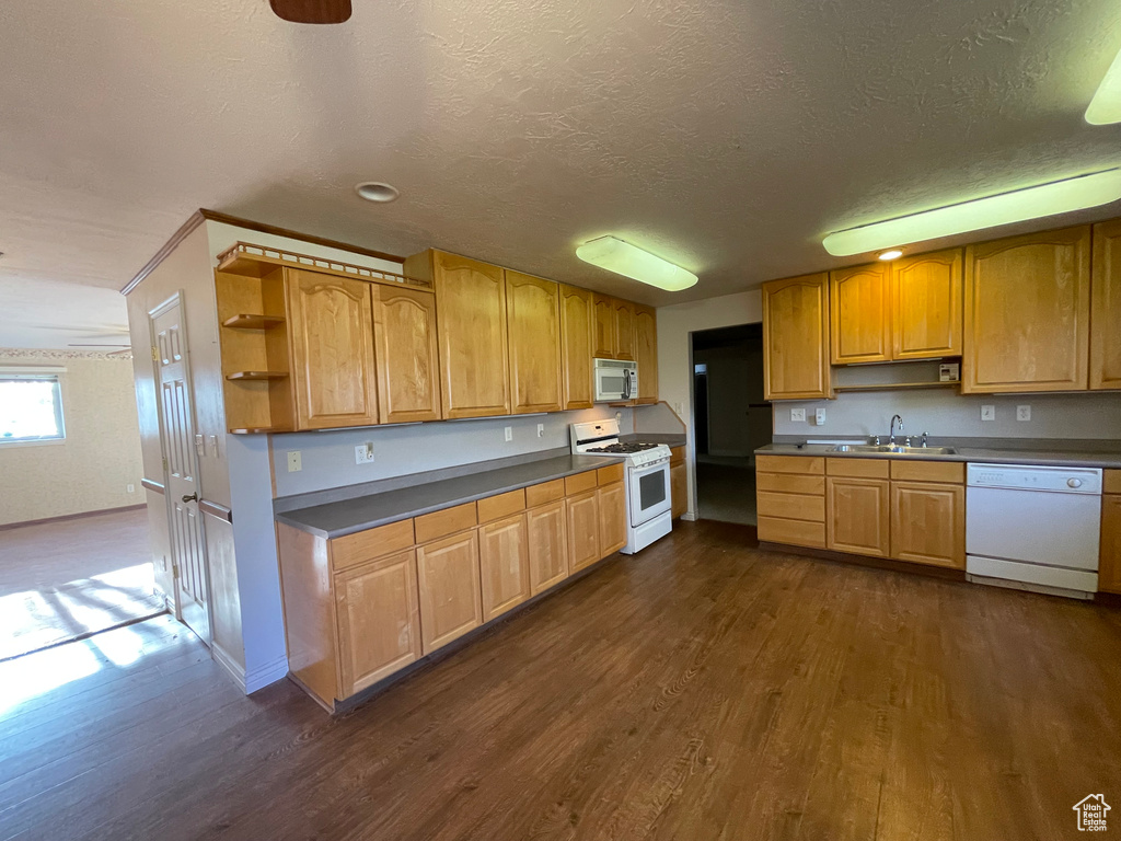 Kitchen featuring white appliances, a textured ceiling, open shelves, dark wood-type flooring, and a sink
