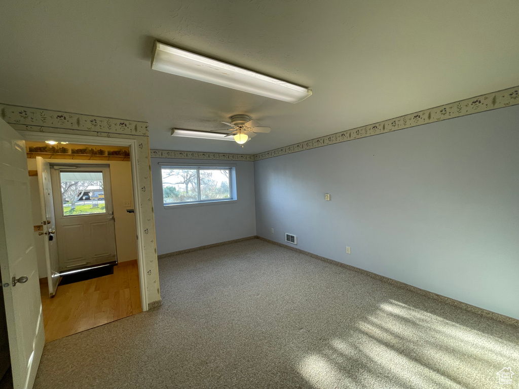 Spare room featuring visible vents, light colored carpet, baseboards, and ceiling fan