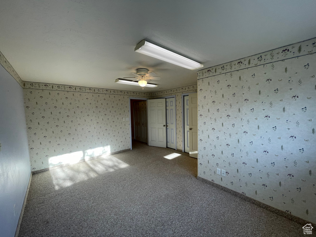 Carpeted empty room with baseboards, a ceiling fan, and wallpapered walls