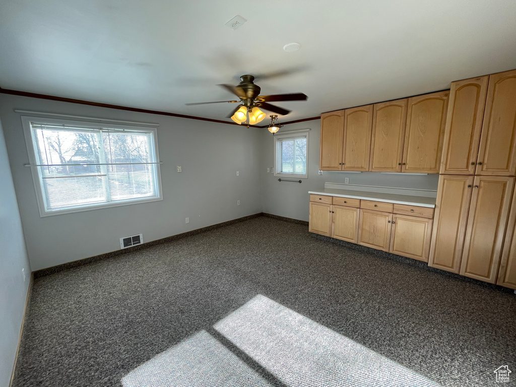 Kitchen with ceiling fan, dark carpet, visible vents, light brown cabinets, and baseboards