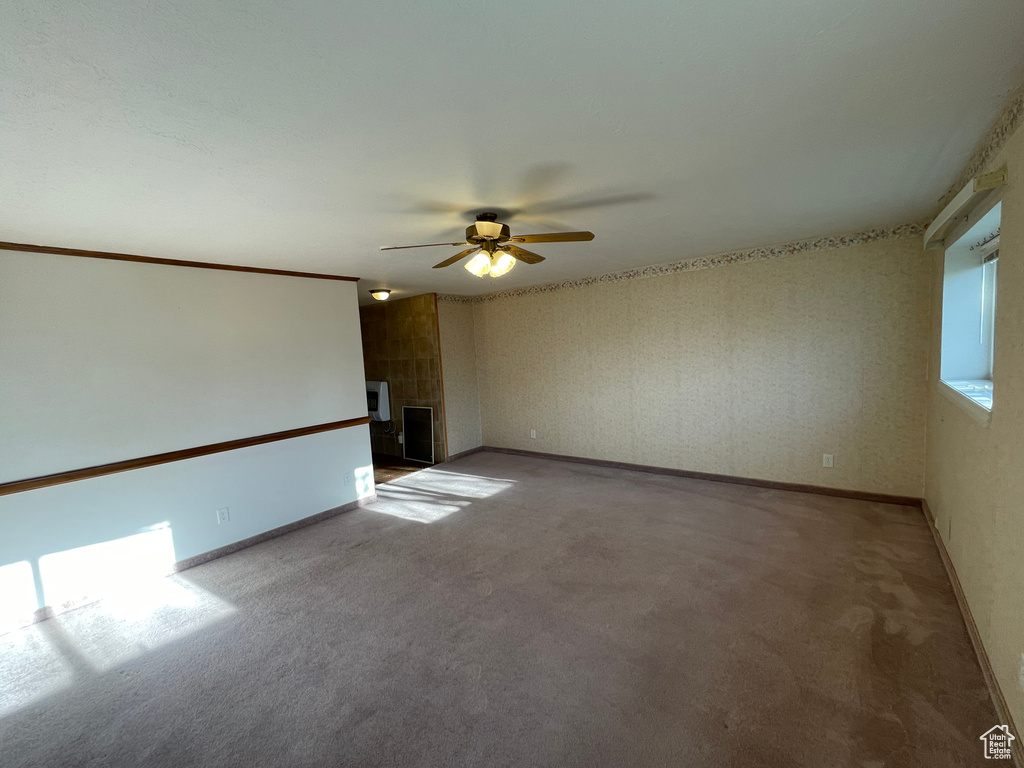 Spare room featuring baseboards, a ceiling fan, a tile fireplace, and light carpet