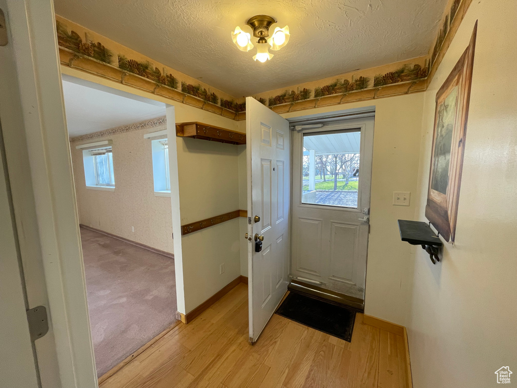 Doorway to outside with light wood-style flooring, a textured ceiling, and baseboards