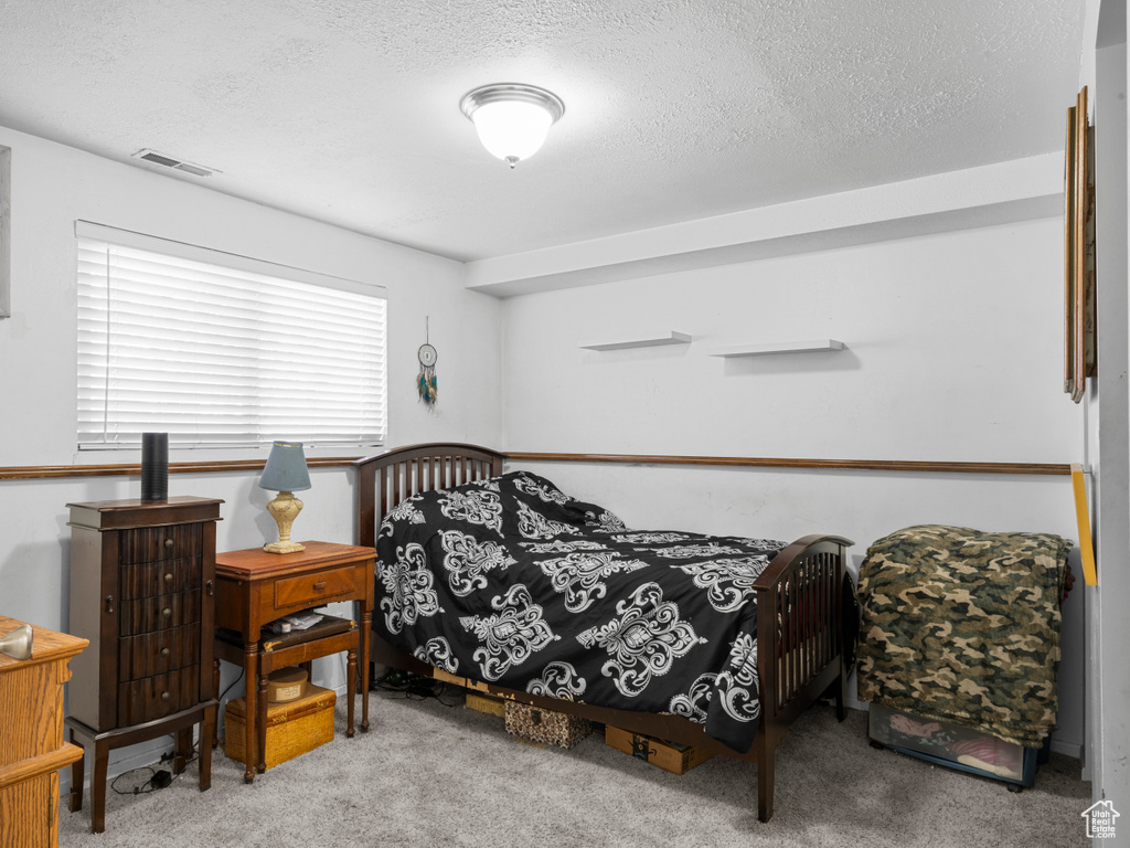 Bedroom with a textured ceiling, carpet flooring, and visible vents
