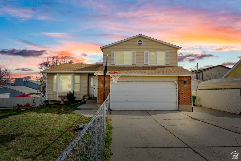 View of front of house featuring a yard, an attached garage, fence, and driveway