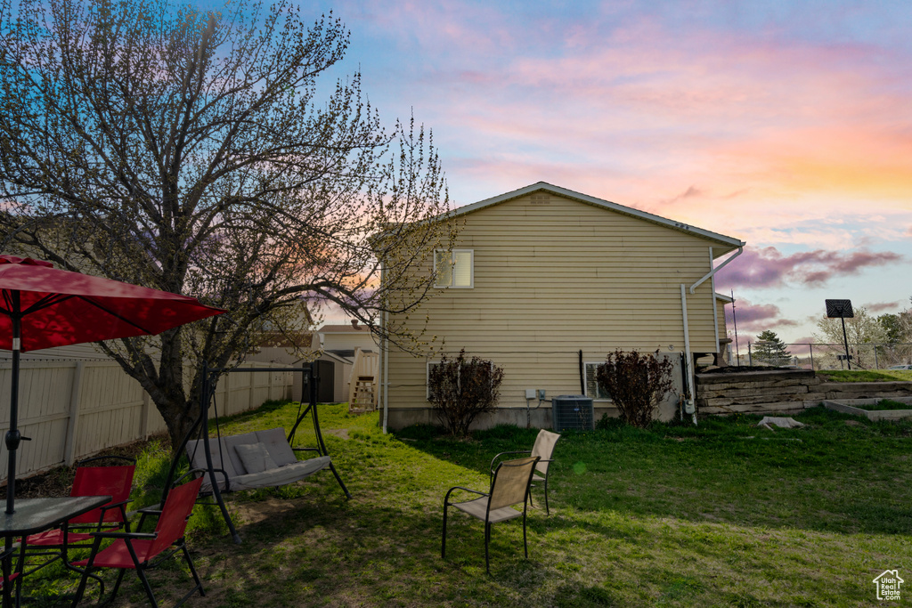 Property exterior at dusk with cooling unit, a yard, and a fenced backyard