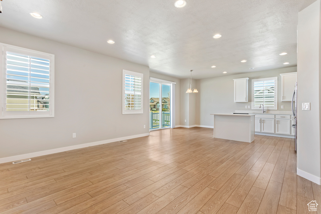 Unfurnished living room with light wood-type flooring, baseboards, recessed lighting, visible vents, and a sink