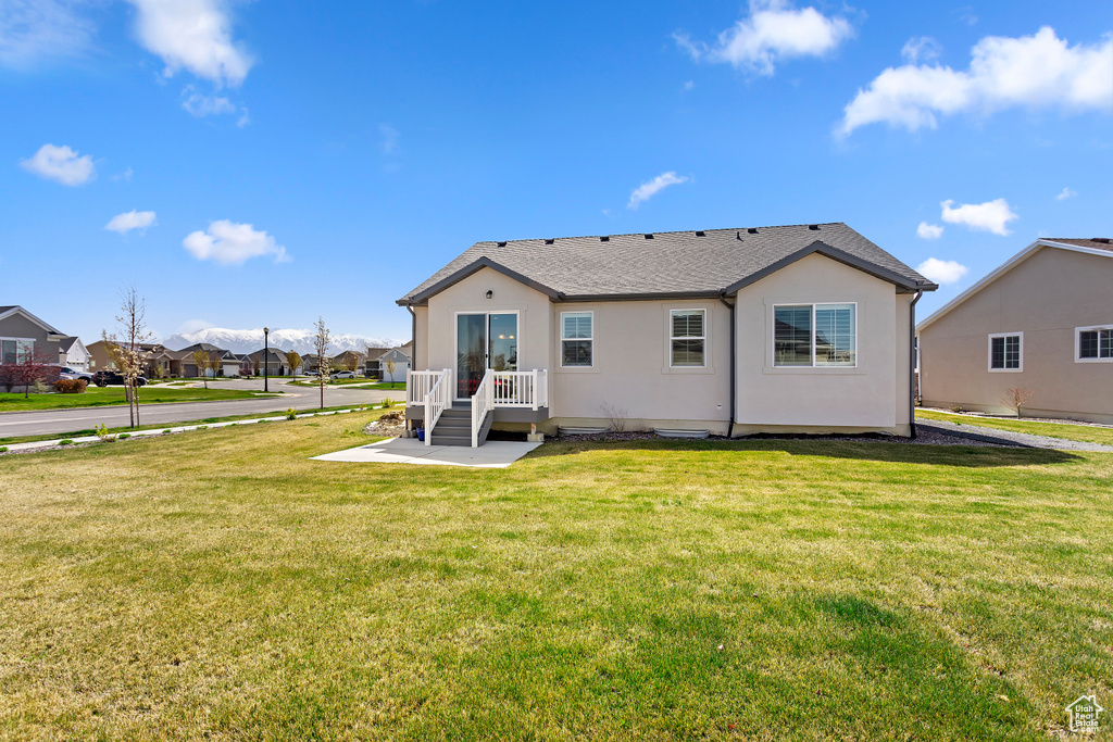Back of house with a residential view, a shingled roof, stucco siding, and a lawn