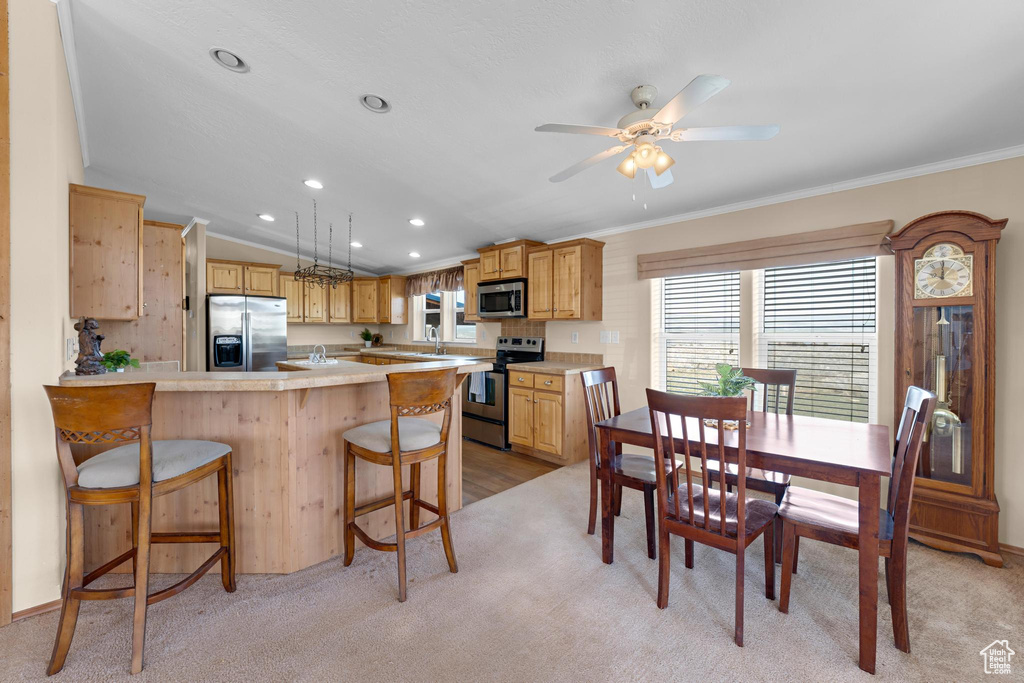 Kitchen with ornamental molding, light countertops, appliances with stainless steel finishes, a kitchen breakfast bar, and a peninsula