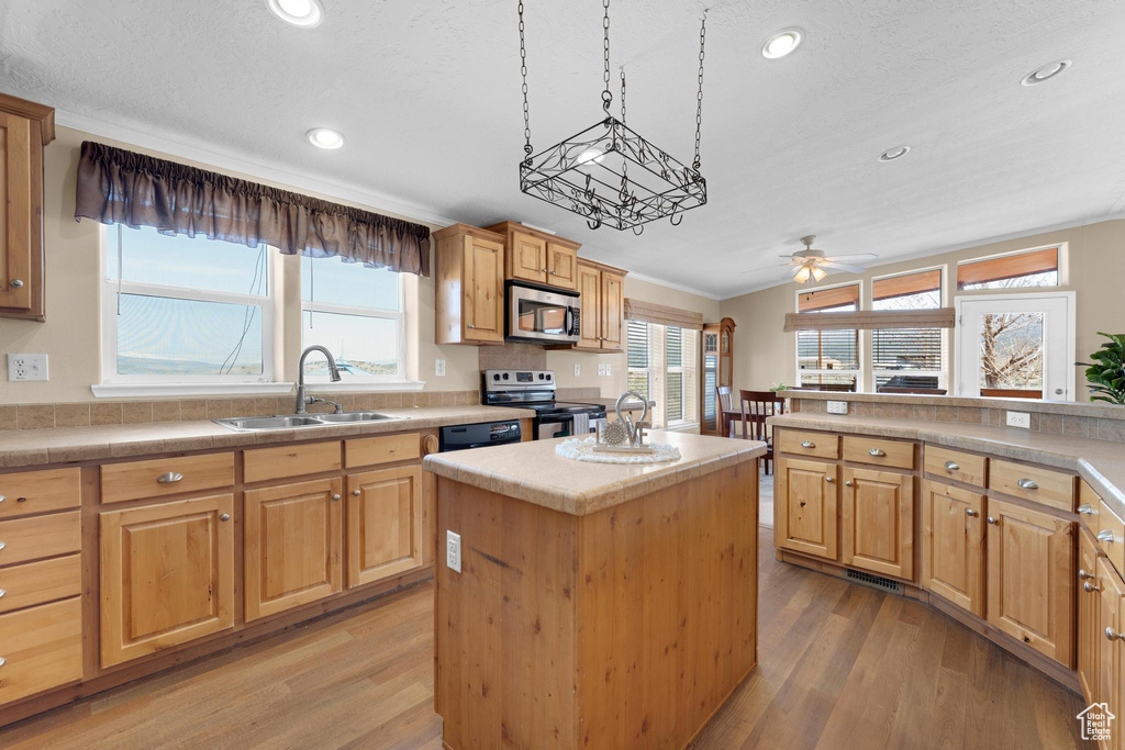 Kitchen featuring light wood-style flooring, a kitchen island, appliances with stainless steel finishes, a sink, and light countertops