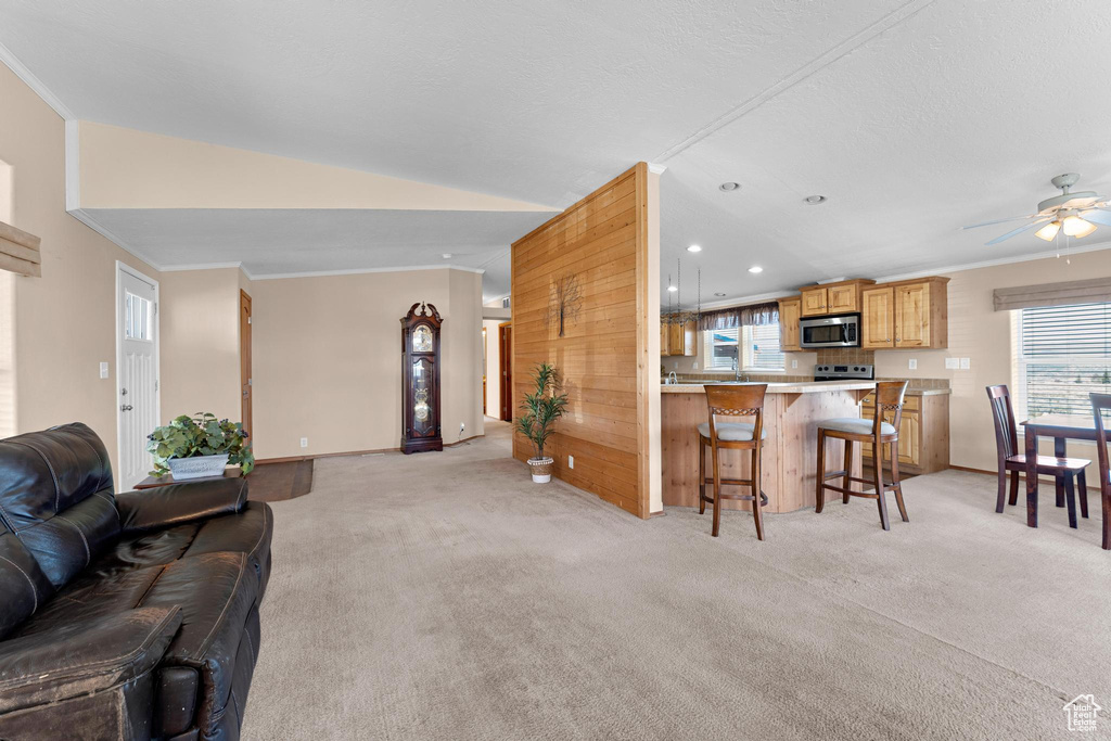 Living room with baseboards, vaulted ceiling, light carpet, crown molding, and a ceiling fan