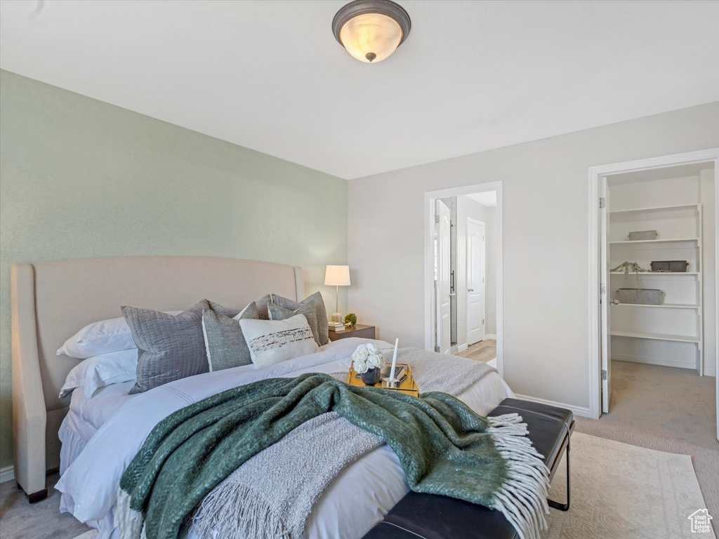 Bedroom featuring light carpet, baseboards, and a walk in closet