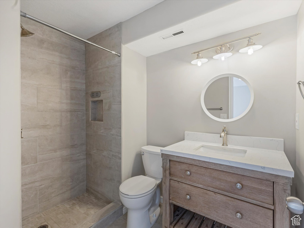Full bath featuring toilet, vanity, a tile shower, and visible vents