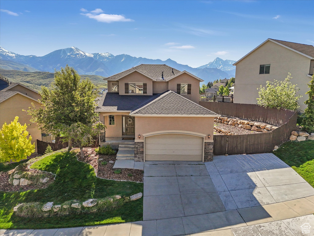 View of front facade featuring stucco siding, a garage, a mountain view, a shingled roof, and driveway