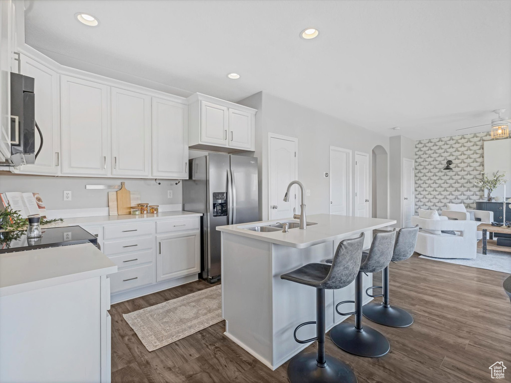 Kitchen featuring white cabinets, arched walkways, stainless steel refrigerator with ice dispenser, a sink, and dark wood-type flooring