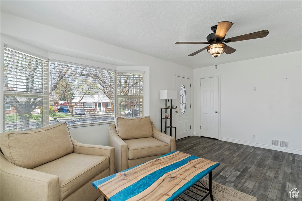Living area featuring dark wood-type flooring, visible vents, baseboards, and a ceiling fan