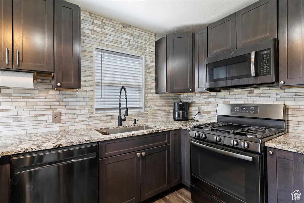 Kitchen featuring dishwashing machine, gas stove, a sink, stainless steel microwave, and decorative backsplash