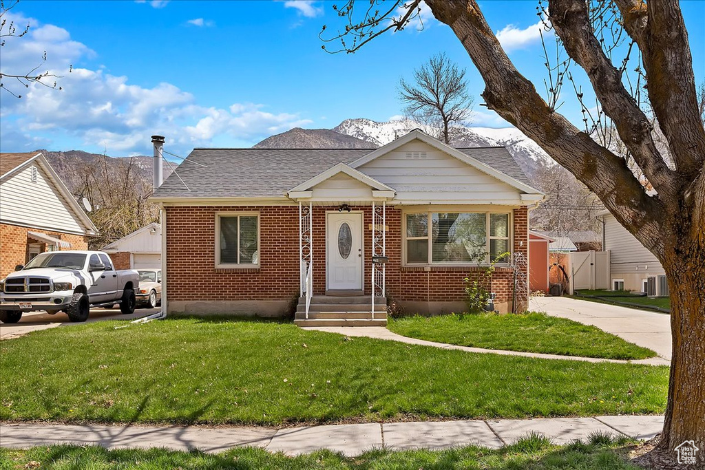 Bungalow featuring brick siding, a mountain view, a front lawn, and roof with shingles