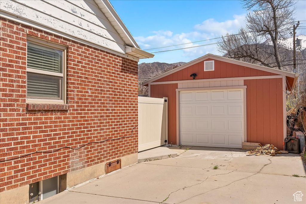 View of side of property featuring concrete driveway, an outdoor structure, a mountain view, brick siding, and fence