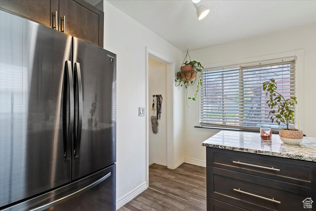 Kitchen featuring dark brown cabinetry, dark wood-style flooring, baseboards, light stone counters, and freestanding refrigerator