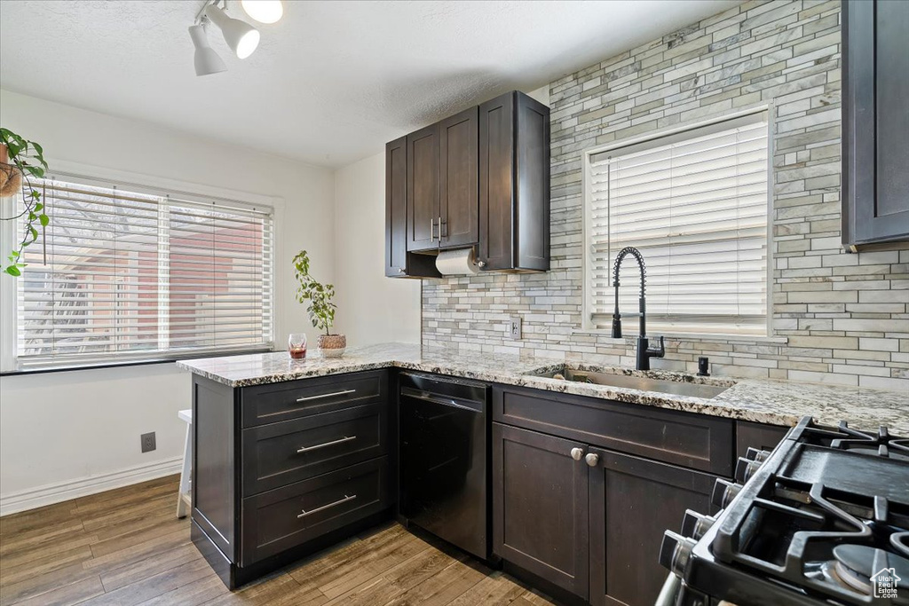 Kitchen with a sink, dark brown cabinetry, dishwashing machine, wood finished floors, and decorative backsplash