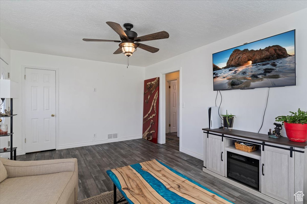 Living room featuring ceiling fan, a textured ceiling, visible vents, baseboards, and dark wood-style floors