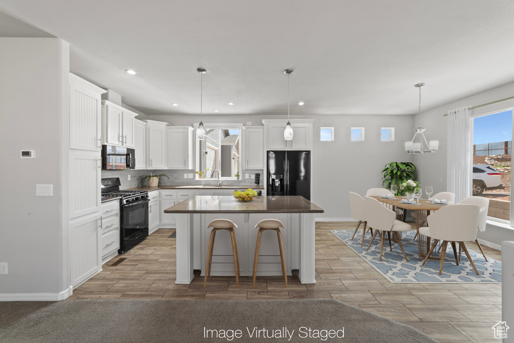 Kitchen featuring a kitchen island, wood finish floors, white cabinets, black appliances, and recessed lighting