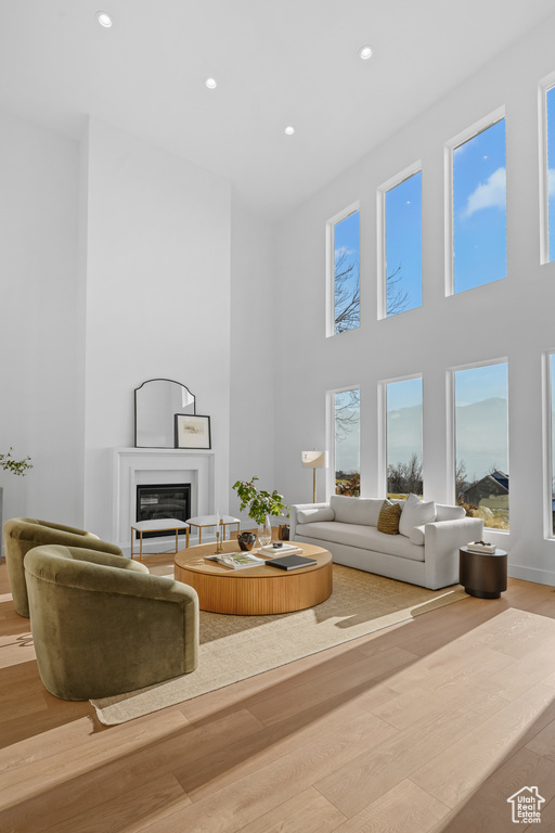 Living area featuring a glass covered fireplace, recessed lighting, a towering ceiling, and wood finished floors