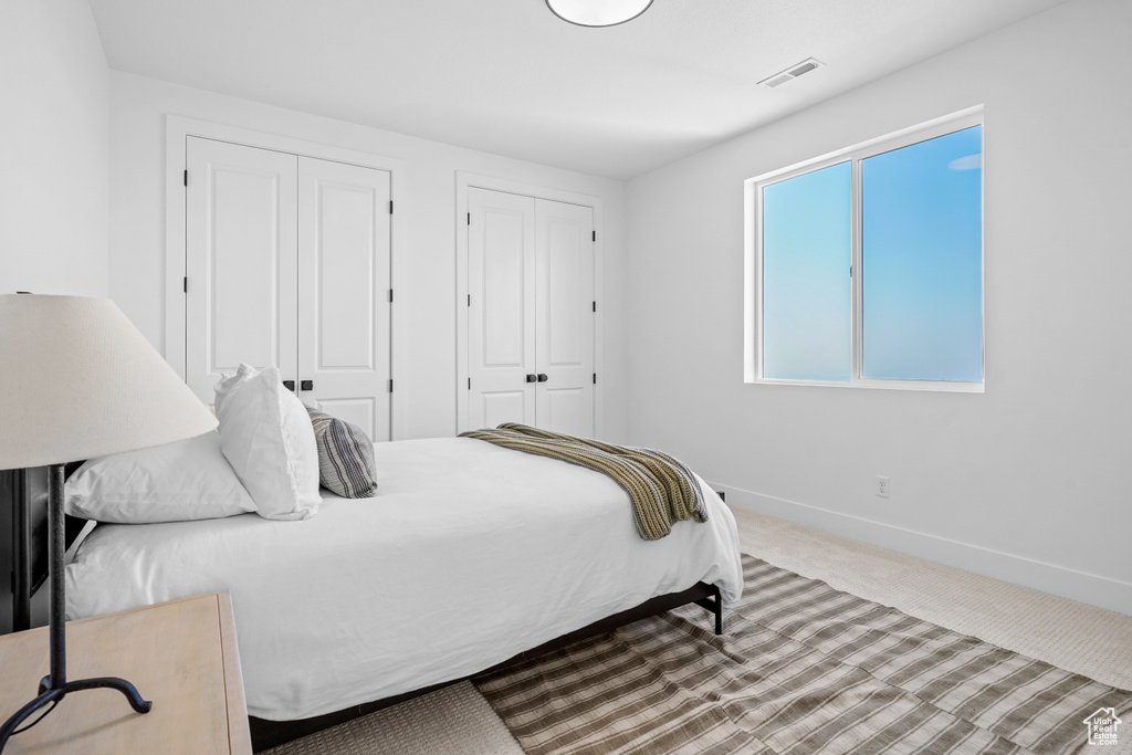 Carpeted bedroom with baseboards, visible vents, and multiple closets