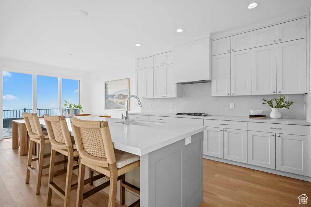 Kitchen with a breakfast bar, custom exhaust hood, light countertops, a sink, and white gas stovetop