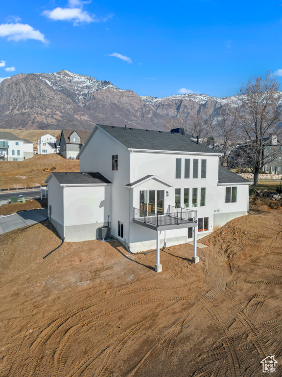 Back of property with a mountain view, roof with shingles, and stucco siding