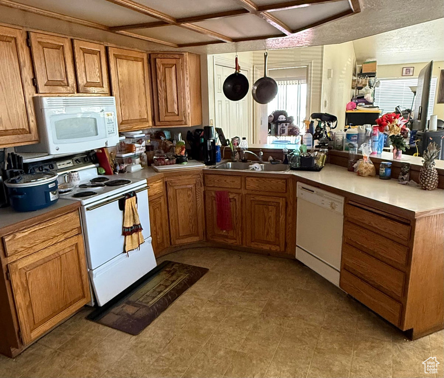Kitchen with white appliances, a peninsula, light countertops, brown cabinets, and a sink