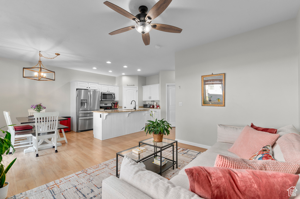 Living area featuring recessed lighting, light wood-type flooring, ceiling fan with notable chandelier, and baseboards
