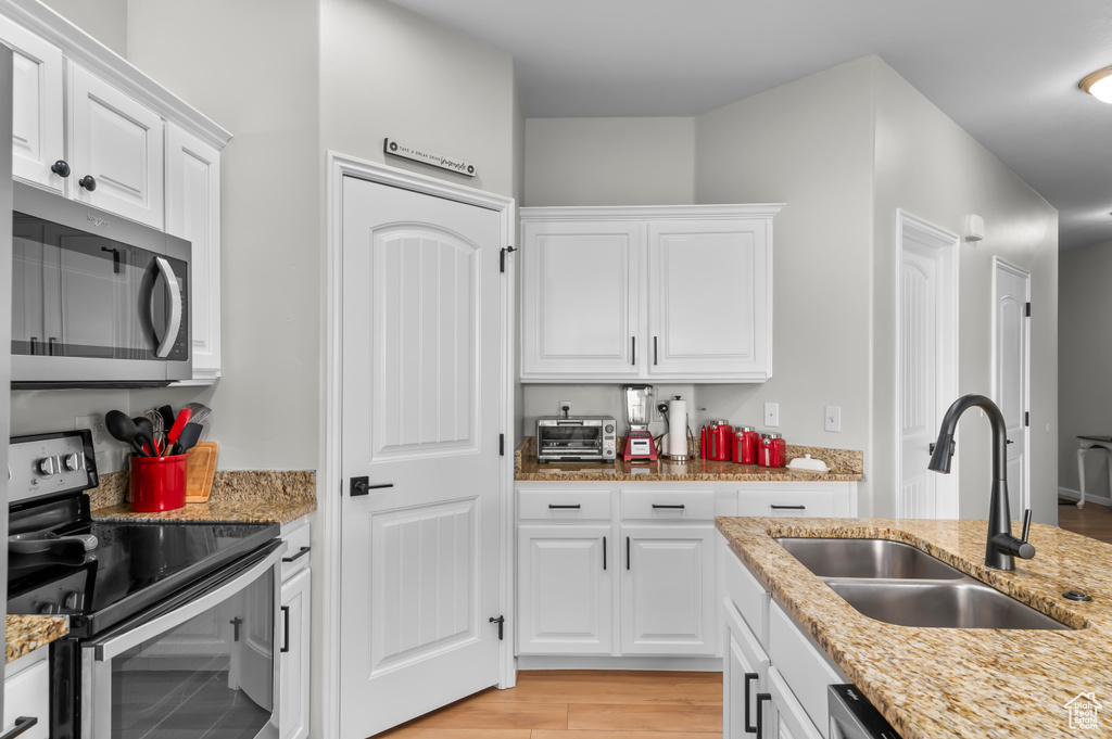 Kitchen featuring light stone countertops, white cabinetry, a sink, and appliances with stainless steel finishes