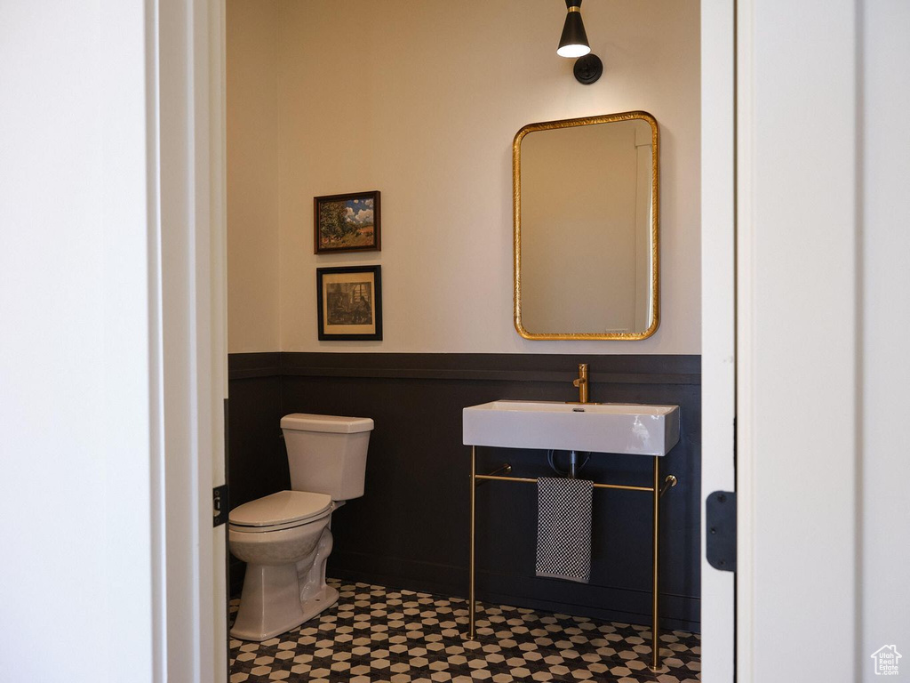 Half bath with a sink, toilet, and a wainscoted wall