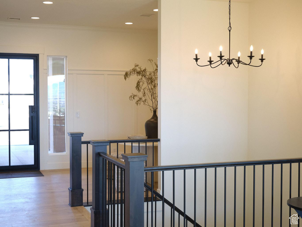 Hall featuring light wood-style flooring, an upstairs landing, a chandelier, and a healthy amount of sunlight