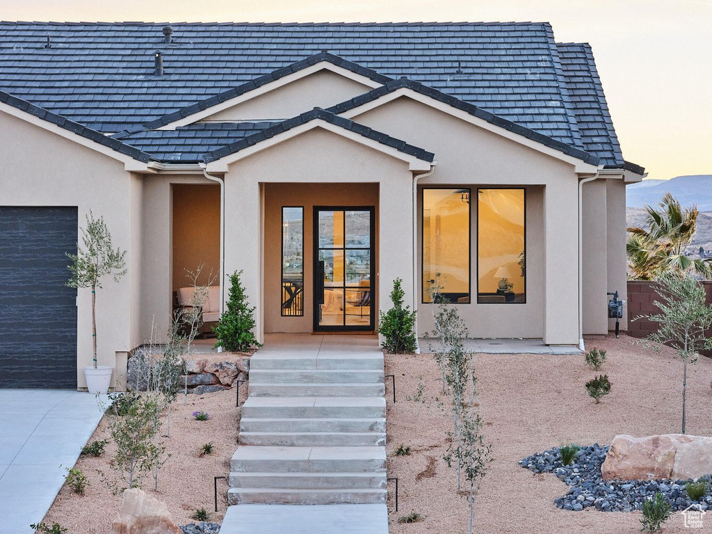 Exterior entry at dusk featuring an attached garage, concrete driveway, and stucco siding
