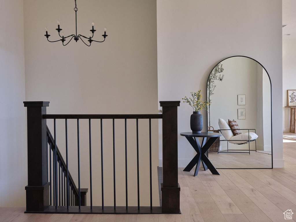 Corridor with arched walkways, a notable chandelier, an upstairs landing, and light wood-style floors