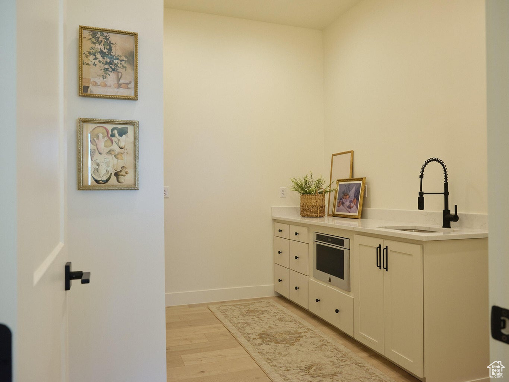 Kitchen featuring baseboards, light countertops, stainless steel oven, light wood finished floors, and a sink