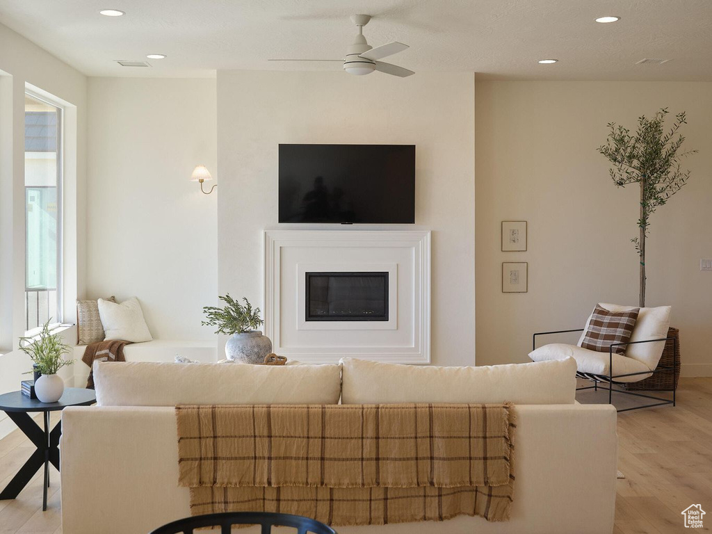 Living room featuring light wood finished floors, ceiling fan, a glass covered fireplace, and recessed lighting