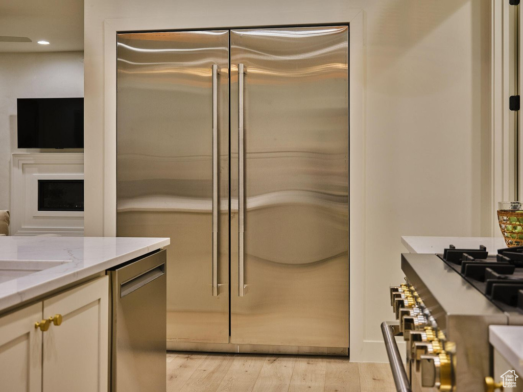 Kitchen with recessed lighting, light wood-style flooring, cream cabinets, light stone countertops, and appliances with stainless steel finishes