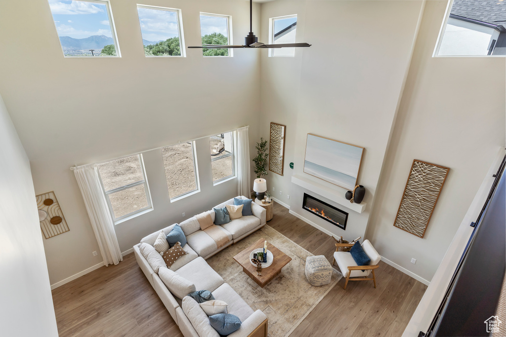 Living room featuring a towering ceiling, a ceiling fan, a glass covered fireplace, and wood finished floors