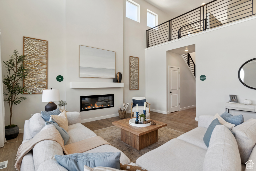 Living area featuring a towering ceiling, wood finished floors, a glass covered fireplace, and stairs