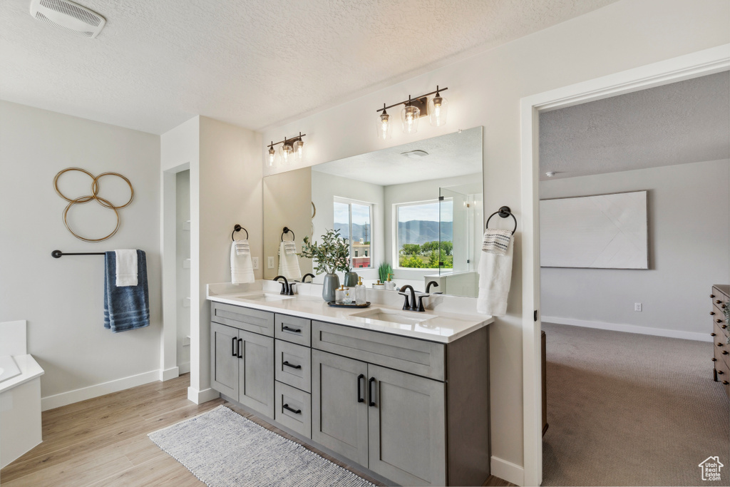 Bathroom with double vanity, a textured ceiling, and wood finished floors